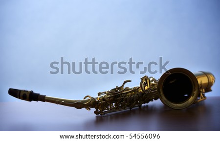 Close-up of backlit saxophone lying on wooden board with narrow focus on buttons, blue background.