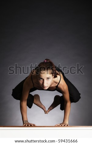 Young pretty woman in yoga crow posture (bakasana), backlit on grey background, front view.
