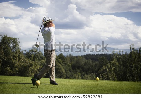 Male golf player teeing off golf ball from tee box, wonderful cloud formation in background.