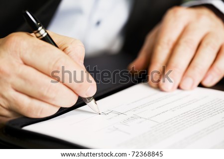 Businessman sitting at office desk signing a contract with shallow focus on signature.