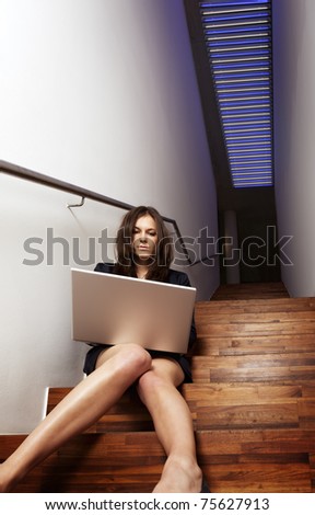 Young pretty businesswoman sitting in modern office staircase with laptop on lap.