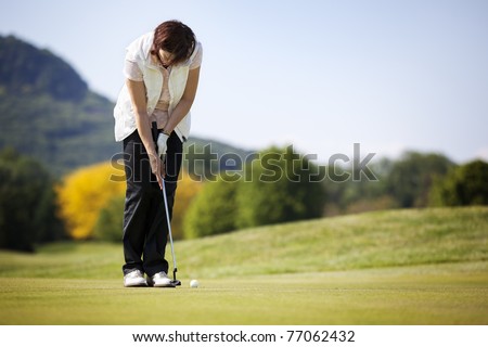 Active senior female golf player putting golf ball on green on beautiful golf course.