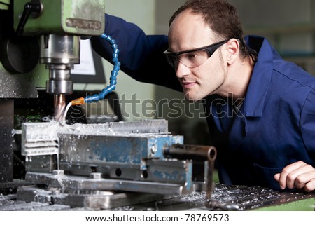 Blue-collar worker with safety glasses at milling machine in workshop.