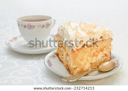 Slice of cake with white whipped cream and scattered almonds on top and a cup of tea