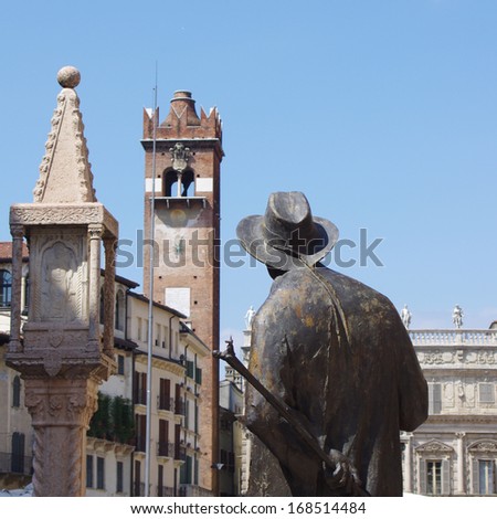 Statue of old man from the back on the background of the famous tower in Verona city, Italy