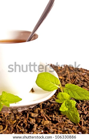 Green tea leaves and a cup of brewed tea with mint leaves