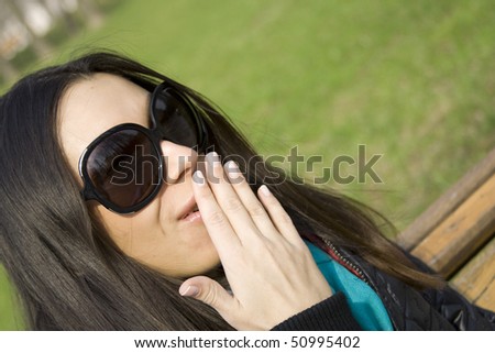 Surprised beautiful woman in the park laughs and covers his mouth with his hand
