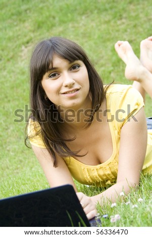 Young Caucasian woman with a laptop in the park on a green grass / meadow