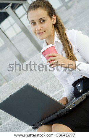 Young, beautiful woman business over coffee in the fresh air sitting on the stairs, office building, next to the laptop