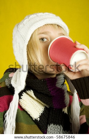 Young woman in a warm sweater, scarf and hat holding a paper cup of coffee. Winter