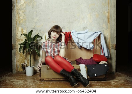 Young beautiful woman on the background of a concrete wall system sits in a big old-fashioned suitcase filled with clothes.