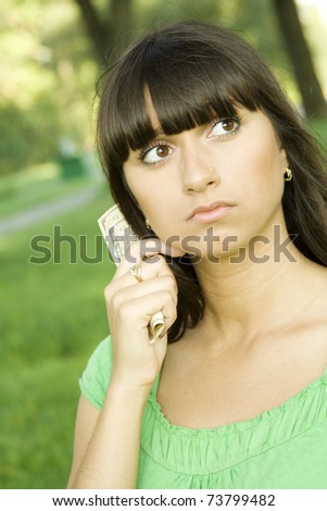 Young woman outdoors holding a cash. Thinks. Little money