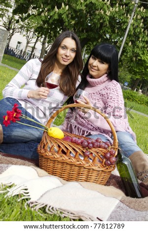 Mother and daughter sitting at a picnic on a blanket drinking wine next to a fruit basket