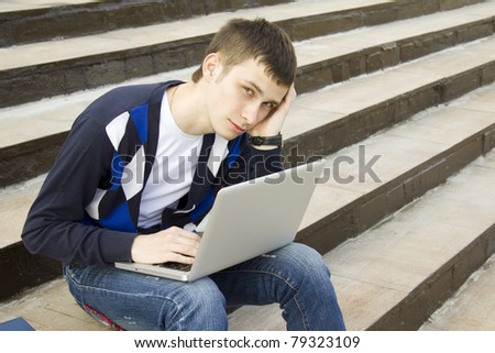 Close-up of a young attractive student on campus sits on a ladder with a laptop. Suffers from headaches