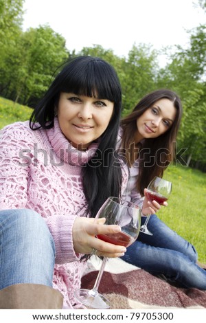 Mother and daughter sitting at a picnic on a blanket drinking wine
