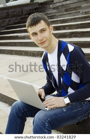 Close-up young attractive student studies on a laptop in a college campus. Sitting on the stairs of the building