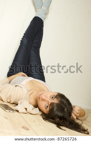 Young woman lying at home on the floor, legs raised up and lean on the wall with a mobile phone