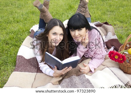 Attractive Mom and daughter, a teenager in a park reading a book and make merry