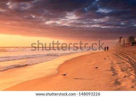 surfers walk along the beach at sunrise (gold coast,qld,australia)