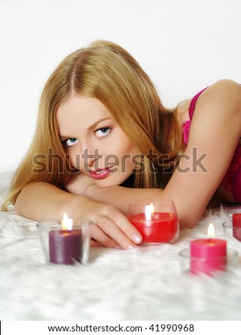 Beautiful young woman with candle, lying on white fur