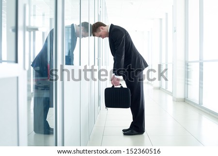 young business man leaned against glass wall in crisis moment