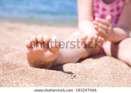 child\'s foot is close to the sandy beach of the seaside resort
