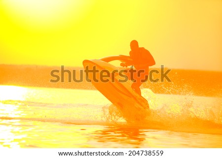 strong man drive on the jet ski above the water at sunset .silluet. spray.