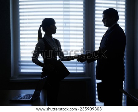 silhouettes of business partners handshake against the window in the office