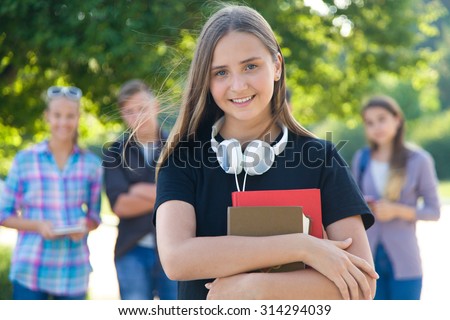 young girl student with books on the background of his friends in the green park