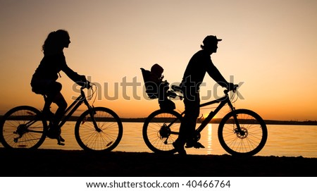 Young family go for a cycle ride on the beach at background sunset