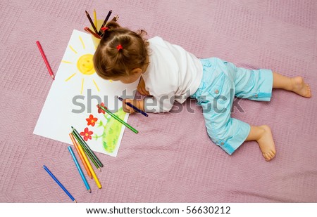 small beautiful girl draws pencils on  paperon lying  on floor