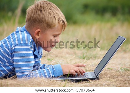 little boy lying grass writes  letter on  laptop