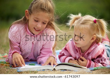 two schoolgirls is  reading  a big  book on the background of green meadows