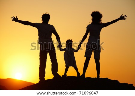 Silhouette of a young family with a child standing on a decline against the bright sun