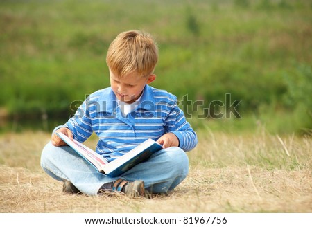 schoolboy is  reading  a big  book on the background of green meadows