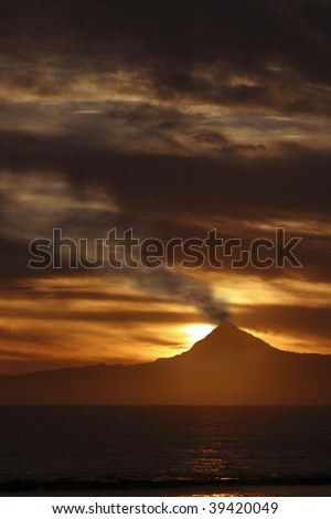 Silhouette of smoking volcano, against sunset clouds