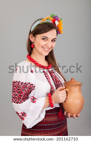 Attractive woman wears Ukrainian national dress is holding a jug isolated on a grey background
