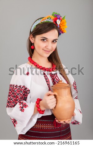 Attractive woman wears Ukrainian national dress is holding a jug isolated on a grey background