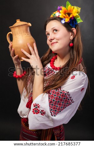 Attractive woman wears Ukrainian national dress is holding a jug isolated on a black background
