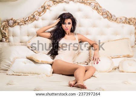 Beautiful and attractive young adult female brunette sensuality woman posing on bed in exclusive apartment