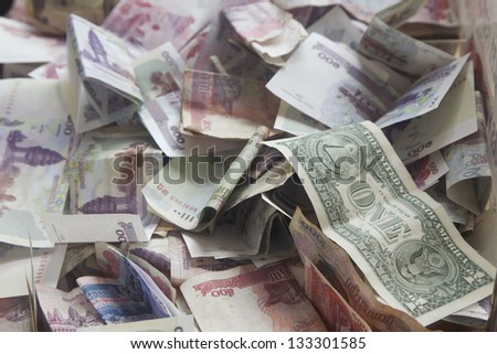 A one US Dollar note on top of a stack of various currencies in a donation box