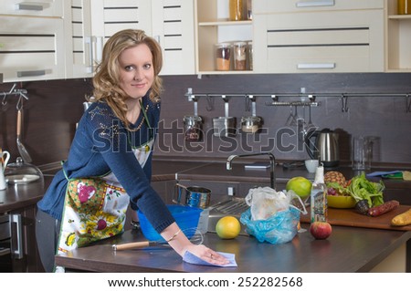 Pretty blonde girl cleans the kitchen with rag and cleanser