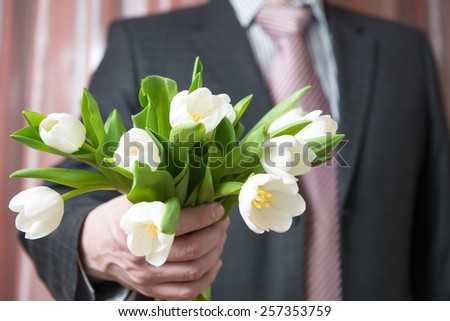 Man - businessman in a suit gives a bouquet of flowers, white tulips