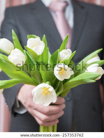 Man - businessman in a suit gives a bouquet of flowers, white tulips
