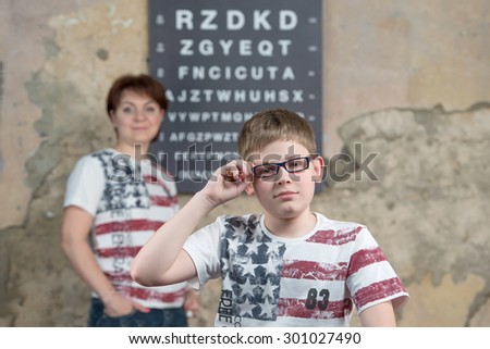 Boy measures the glasses on background mother and a table for sight check