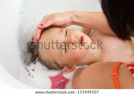 A toddler getting a hair wash in the bath tub by he\'s mother, he is relaxed with he\'s eyes closed.