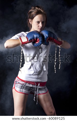 Sexy young woman with blue boxing gloves isolated on a black background with smoke behind her.
