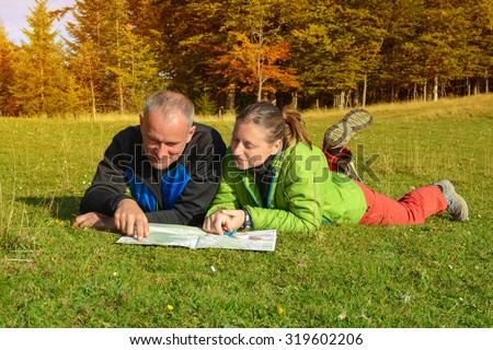 Cheerful hikers are  planning their route. Smiling man and woman are lying in the autumn forest. Hikers couple with map.