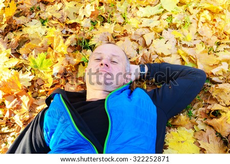 Happy man enjoying life in the autumn park. Active man relaxing on fallen leaves in a beautiful  autumn day.