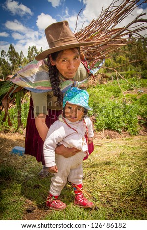 RAQCHI PERU -JANUARY 15: Unidentified Quechua indian woman and child carrying wood and living inside Raqchi Ruins, Peru on January 15, 2013. Raqchi Ruins a popular destination for tourism in Peru